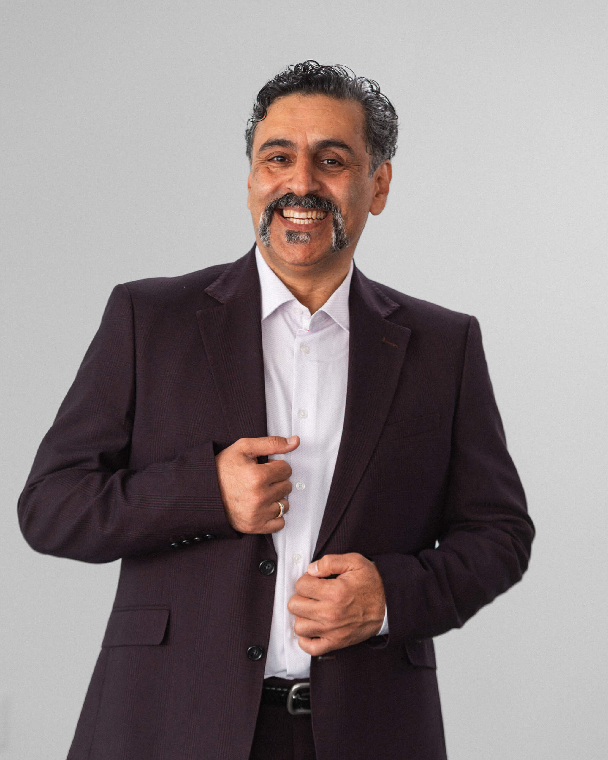 Alireza Sedghi Taromi, un hombre de pelo oscuro y bigote, aparece sobre un fondo claro con un traje oscuro y camisa blanca, sonriendo mientras se abrocha la chaqueta.
