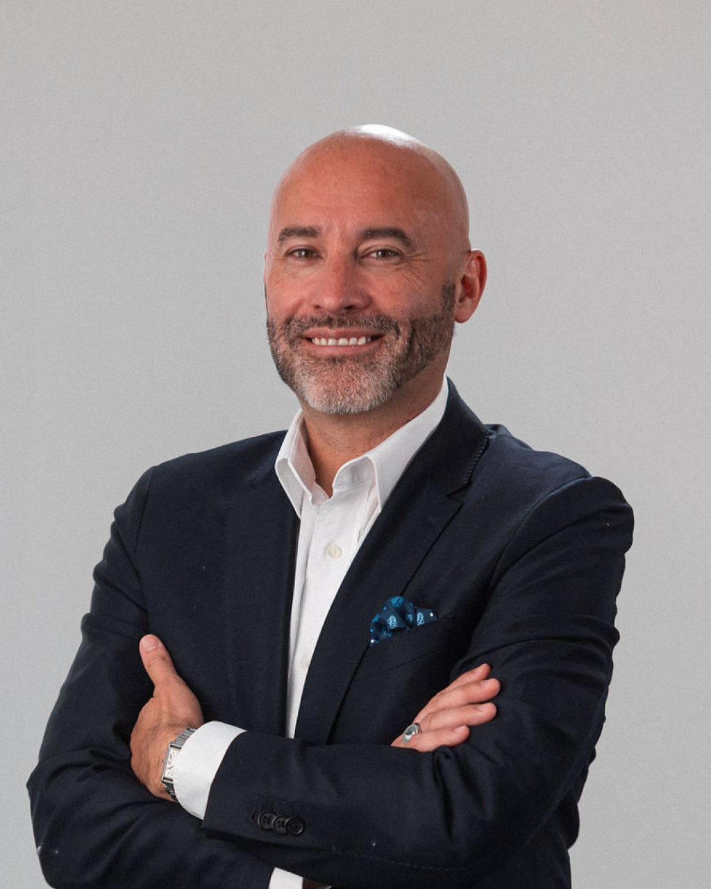 Jason Walker, psicólogo con calva y barba, de pie, con los brazos cruzados, traje oscuro y camisa blanca, sonríe confiado sobre un fondo liso.