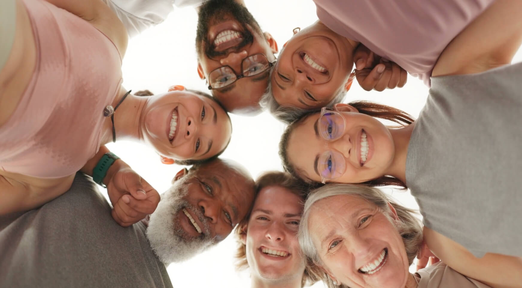 Un grupo de siete personas de diferentes edades forma un círculo, sonriendo y mirando hacia la cámara.